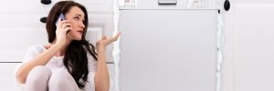 woman on the phone sitting in front of a dishwasher leaking suds