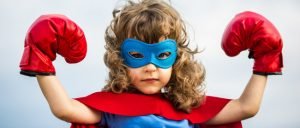 Superhero kid wearing boxing gloves against blue sky background. Girl power concept