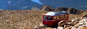 Pikes Peak Cog Railway car traveling doen from top of Pikes Peak mountain top in Colorado on sunny summer morning with mountains and lake in distance