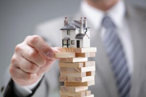 man playing Jenga with a house on top of stack